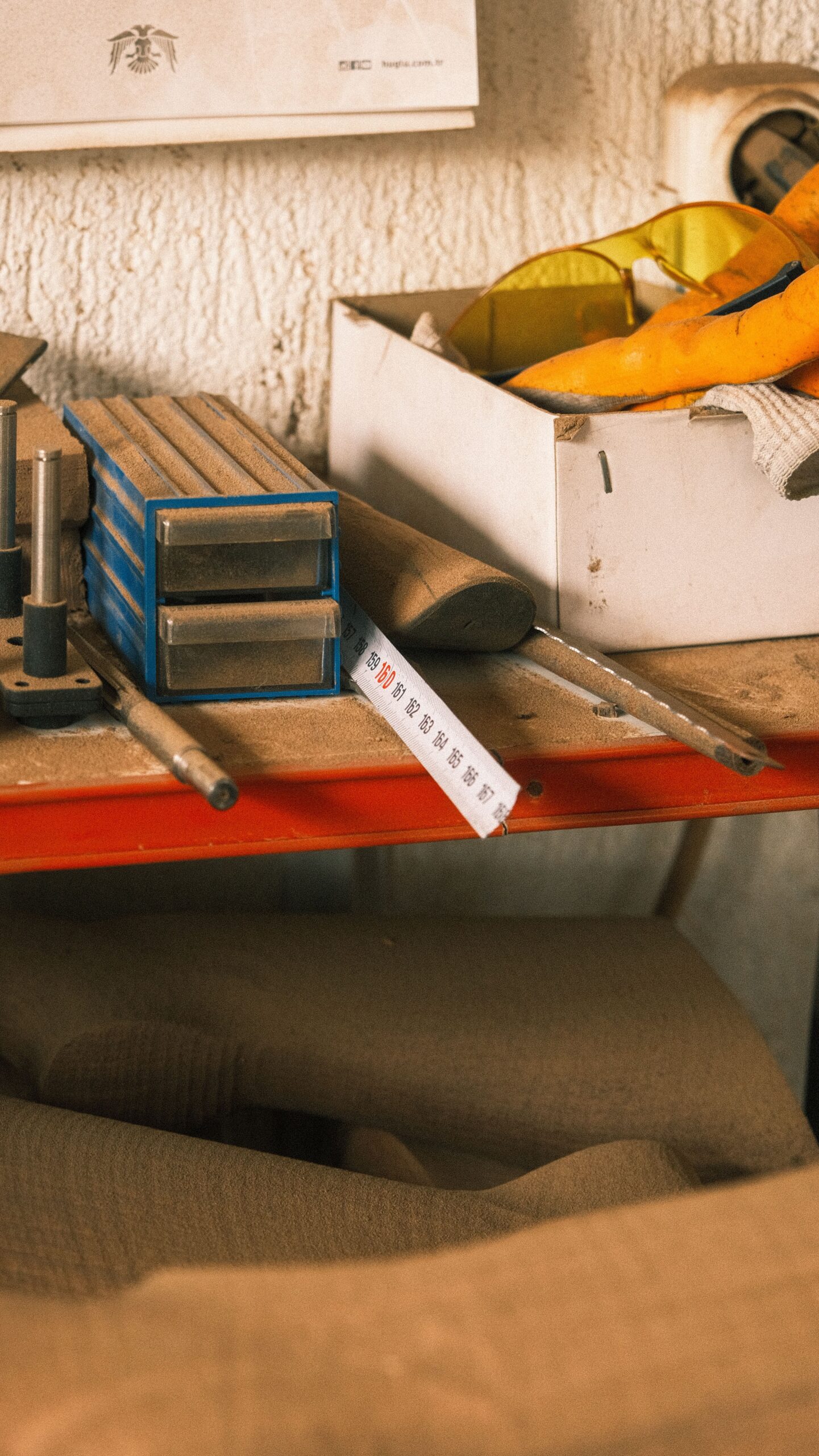 A warm-toned workshop corner featuring tools, measuring tape, and protective gear on a shelf.