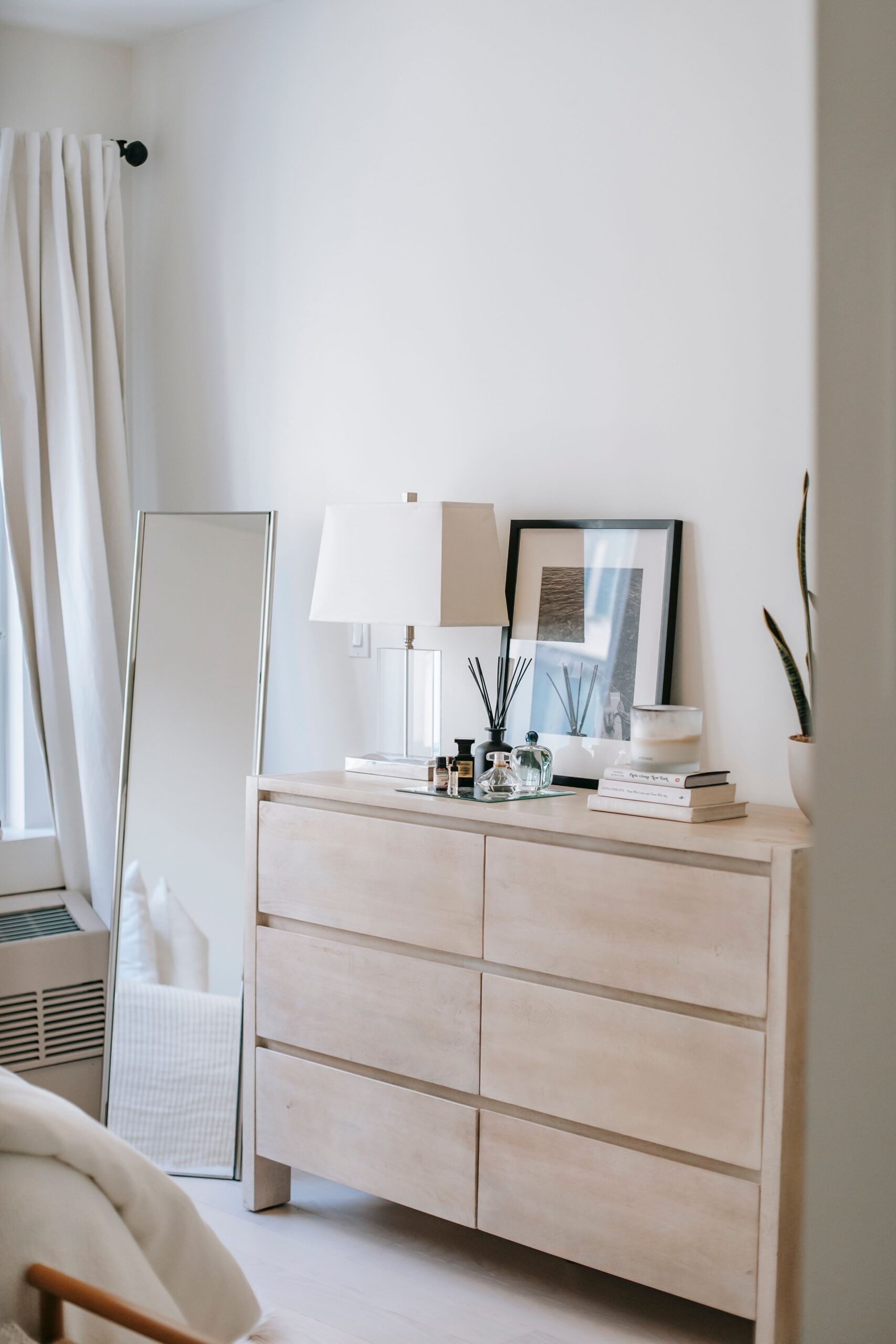 Decorative bottles and photo on wooden commode near rectangular shaped mirror on floor at home